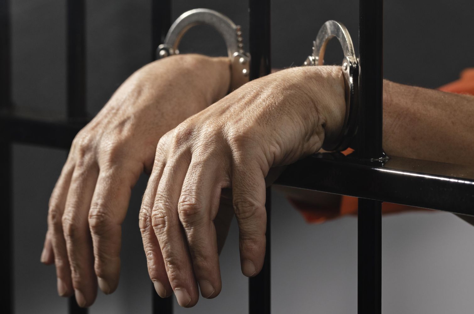 4ghukum catrawarta Hands in metal handcuffs gripping a jail cell bars orange jumpsuit visible in background