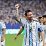 Argentine soccer players celebrate on the field as the captain raises a clenched fist in triumph crowd in the background