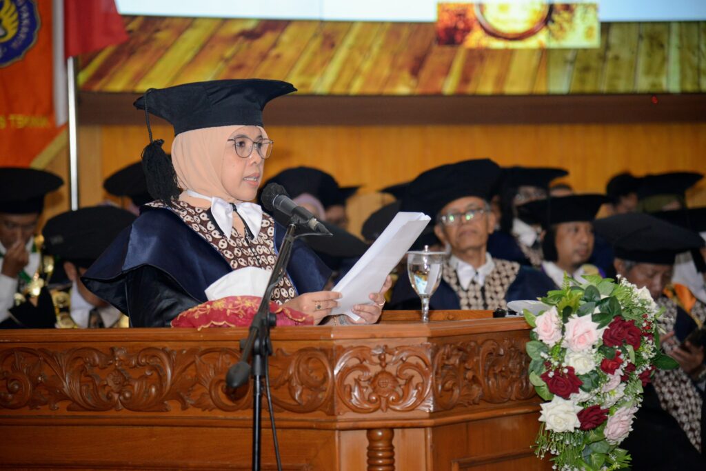 5 prof dyah catrawarta Female graduate in hijab and cap speaks at a podium during a graduation ceremony with a floral arrangement in the foreground