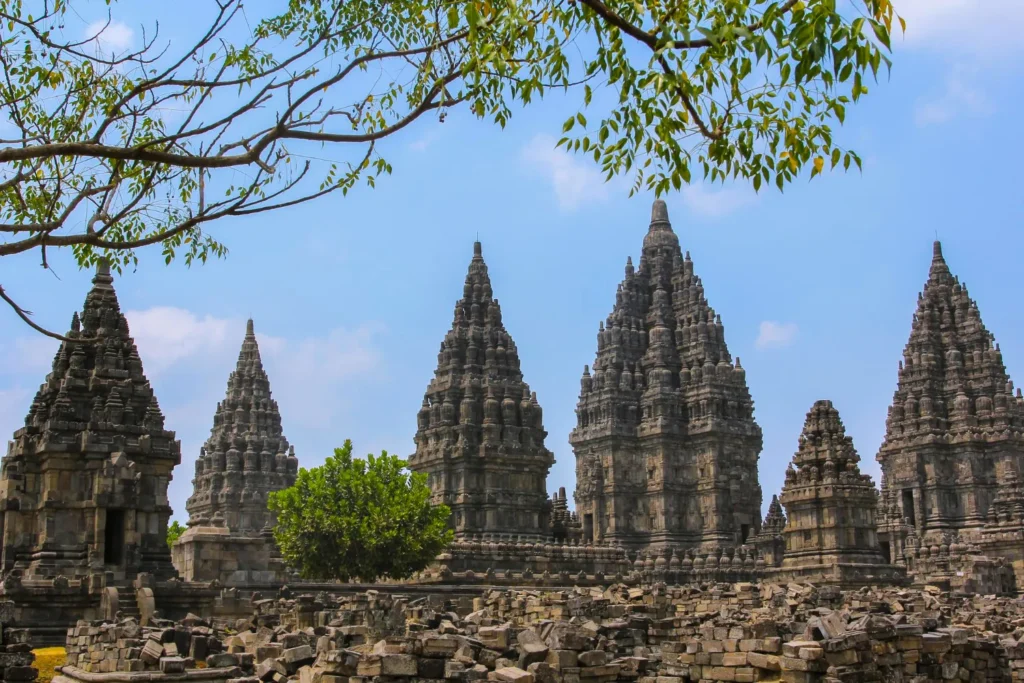 5fa8f379b708448c8e9d0b543a55479562de3470 catrawarta Ancient gray stone temple complex with tall central spires under a blue sky surrounded by scattered stones