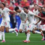 Morocco national team players celebrate a goal running across the field in white kits with green badges