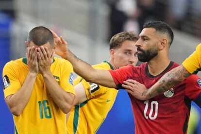 A tense moment on the field: a yellow-jerseyed player (number 16) covers his face as teammates restrain him while a red-jerseyed player (number 10) reaches toward him.