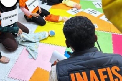 Suspects kneeling on colorful foam mats with signs reading 'TERSANGKA' and numbers, under police supervision.