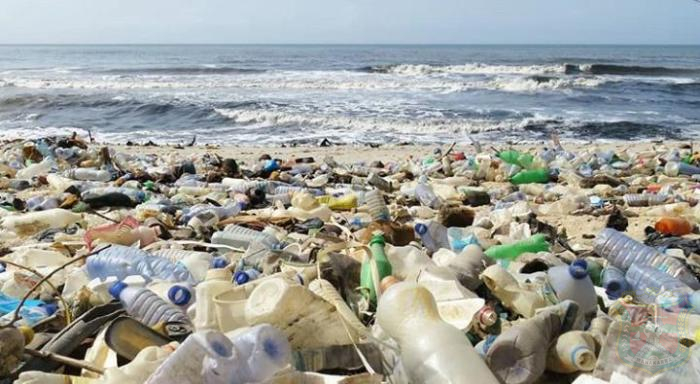 Polusiplastik catrawarta Beach covered in plastic waste and bottles strewn across the sand with waves in the background showing pollution along the shoreline