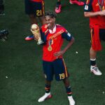 Soccer player in red jersey with campeones holding a golden trophy and wearing a gold medal celebrating on the field
