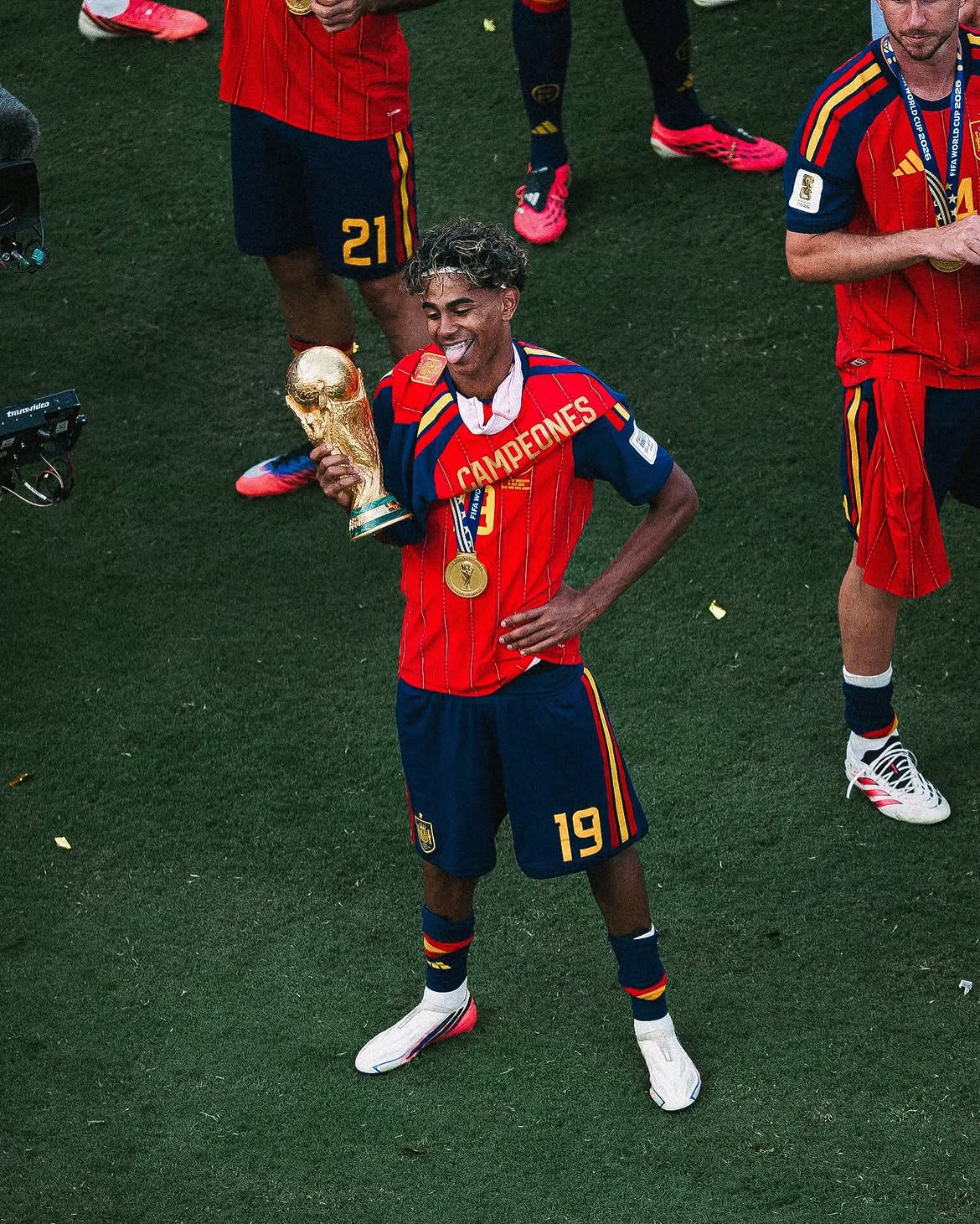 Lamine yamal jadi pemain yang berhasil mengawinkan piala euro dan piala dunia 2026 catrawarta Soccer player in red jersey with campeones holding a golden trophy and wearing a gold medal celebrating on the field