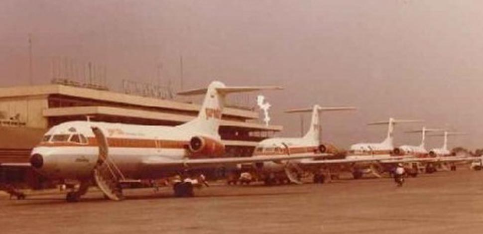 7a catrawarta Row of vintage white and orange rearengine airliners parked on a tarmac with a mobile staircase at the first plane nearby ground crew