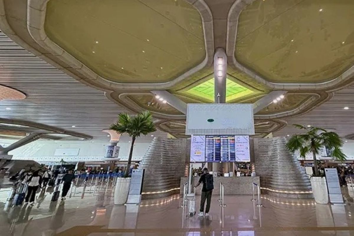 7gbandara1 catrawarta Modern airport check in hall with a central info board curved staircases and travelers queuing in line palm trees visible in the background