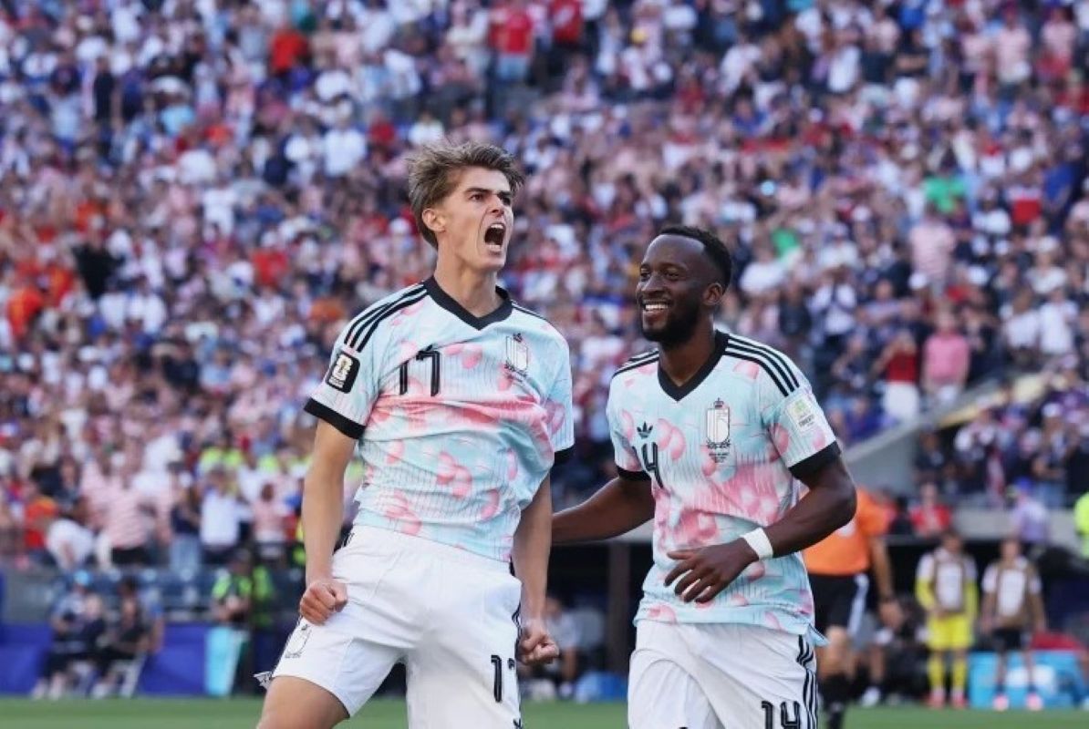 7gbelgia1 catrawarta Two soccer players in pale pink camouflage jerseys celebrate a goal on the field as the crowd cheers