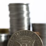 Close up of a large silver coin in the foreground with an eagle design and blurred stacks of coins in the background