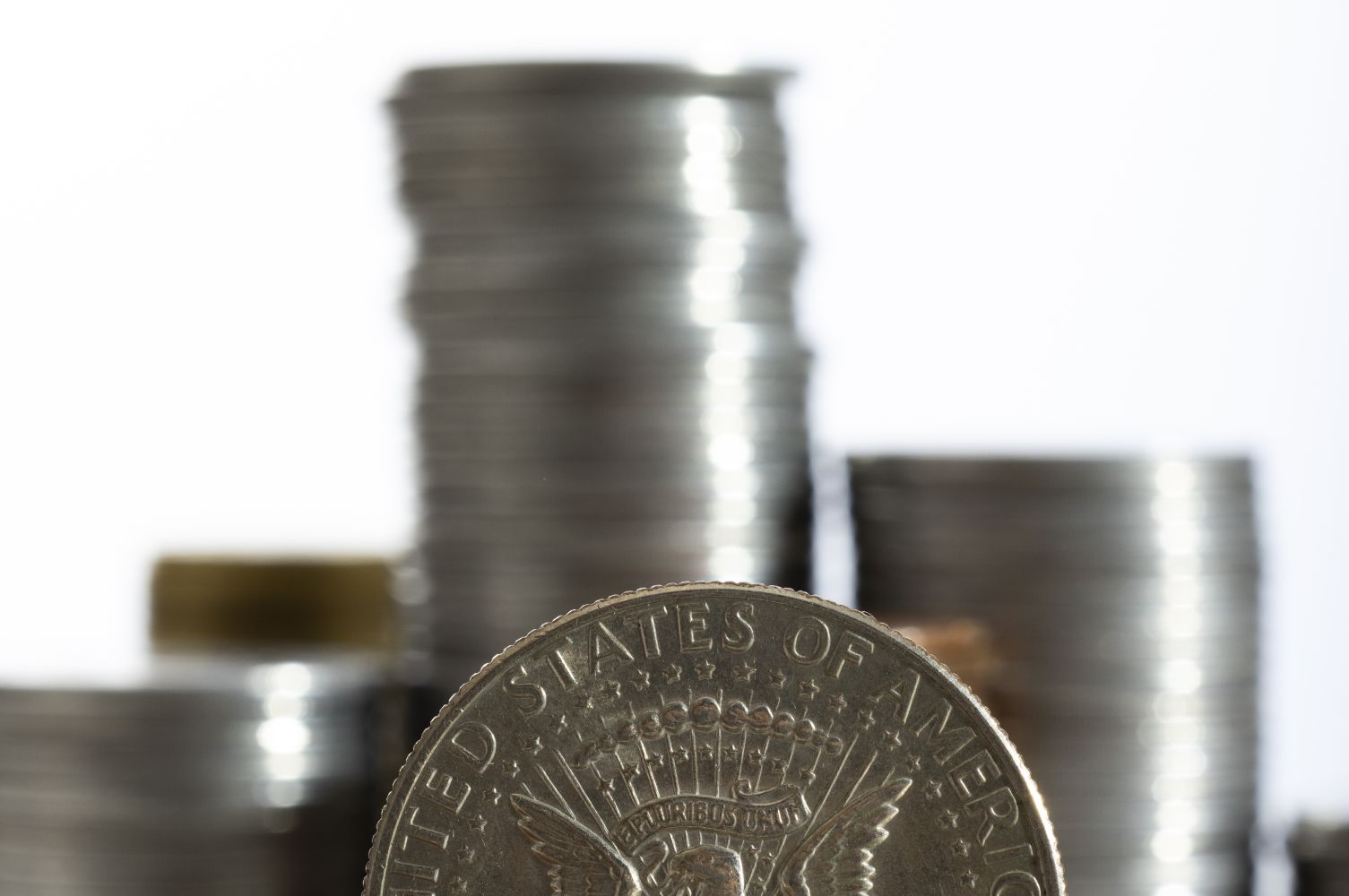 7gdolar catrawarta Close up of a large silver coin in the foreground with an eagle design and blurred stacks of coins in the background