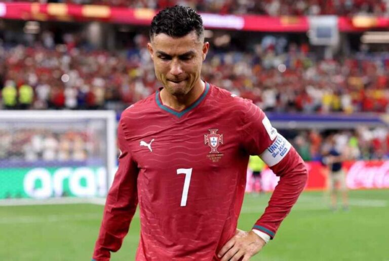 Portuguese footballer wearing red jersey with number 7 on a football pitch, crowd in the stands behind him.