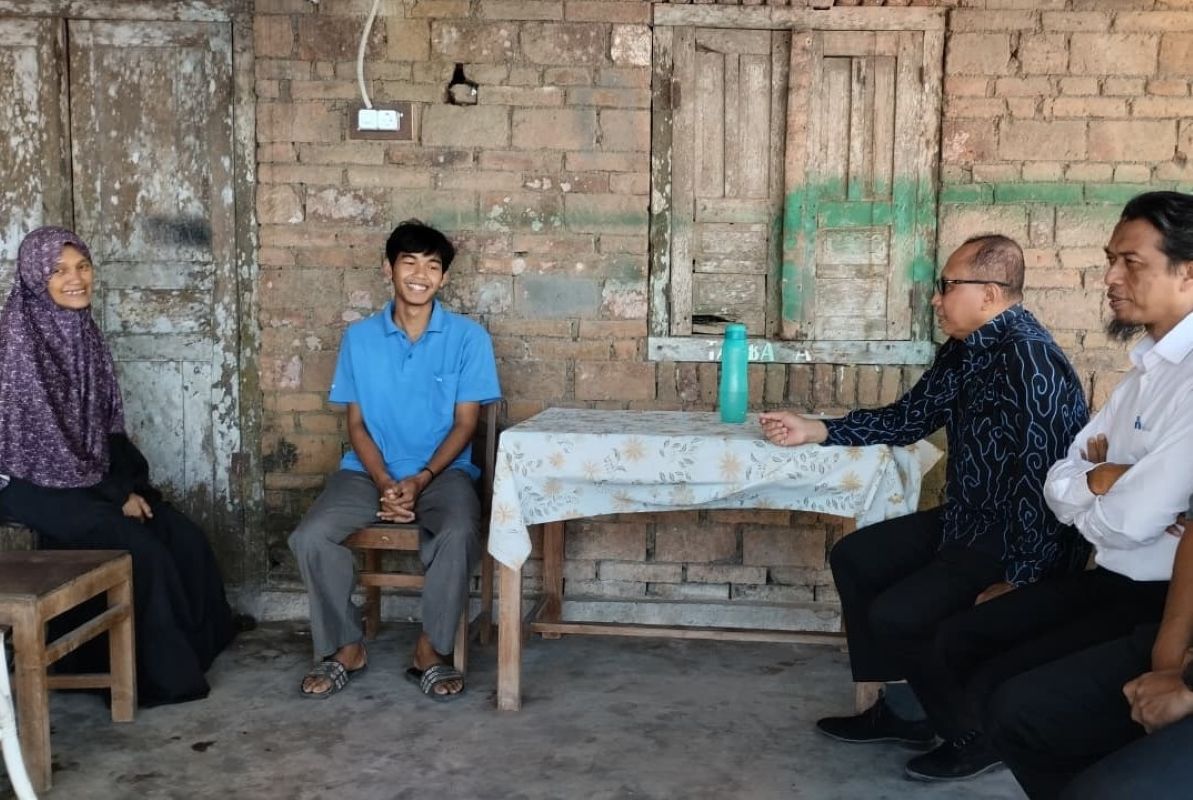 8garifin catrawarta A young man in a blue polo sits smiling between a woman in a purple hijab and three men at a wooden table in a brick walled room with a turquoise water bottle on the table