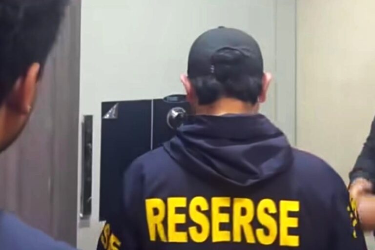 Back view of a person in a dark jacket with large yellow 'RESERVE' text on the back, indoors near equipment.