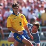 Soccer player in a yellow jersey 2 sprinting with the ball while a blue jersey opponent challenges him