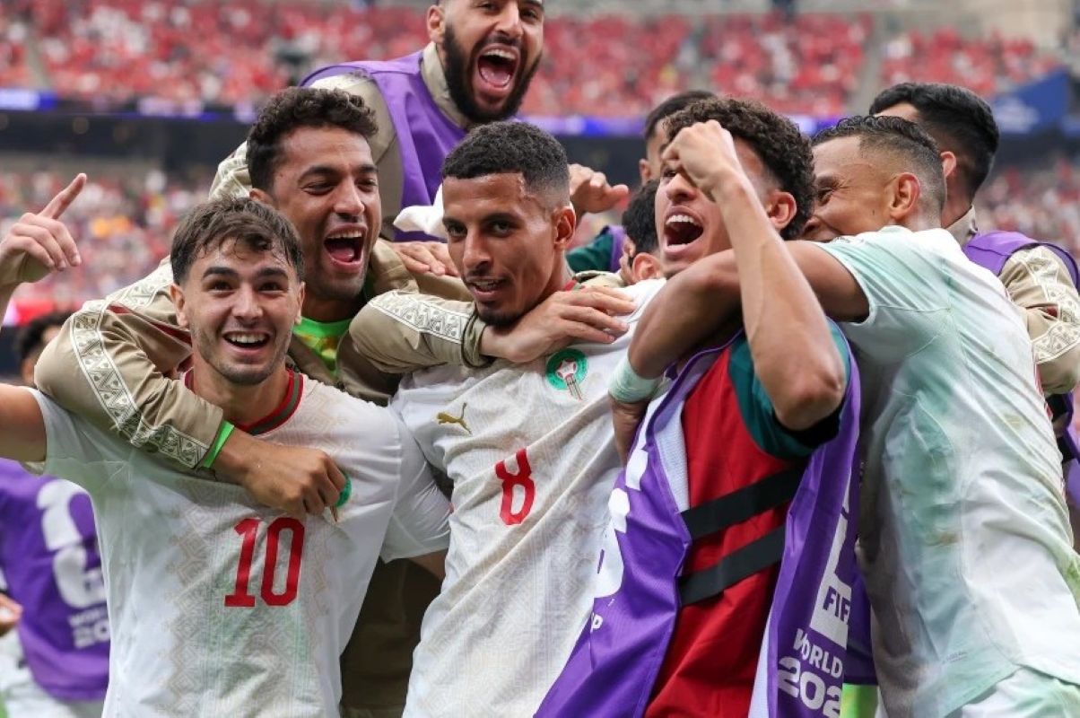 9gmaroko1 catrawarta A group of soccer players in white jerseys celebrate together on the field arms around each other in joy after a victory
