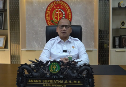 Man in a white uniform shirt sits at a dark carved desk in a formal office with a government emblem behind him