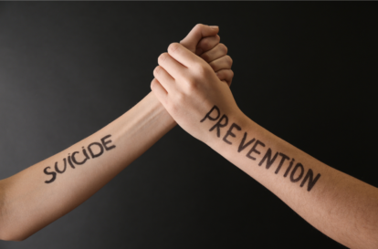 Two forearms clasped in a handshake, with 'SUICIDE' on one arm and 'PREVENTION' on the other, signaling support and awareness for prevention.",