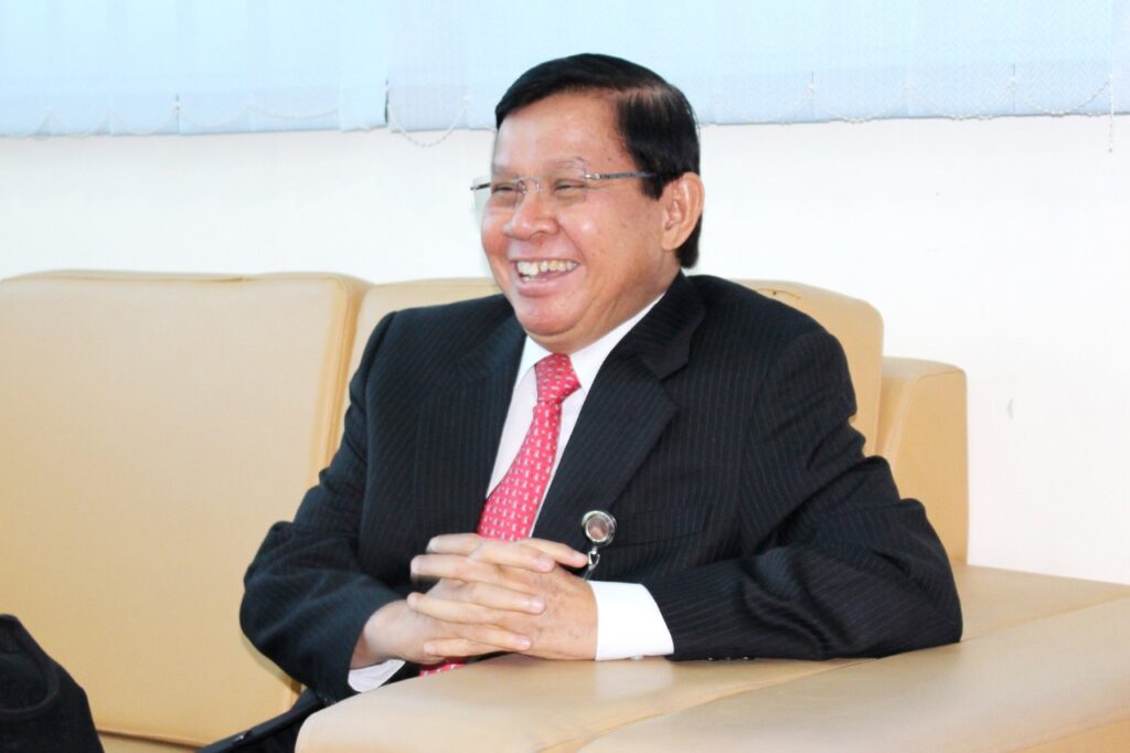 Faslijalallaughing catrawarta Smiling man in a dark pinstripe suit and red tie sits on a beige couch laughing during a meeting room chat
