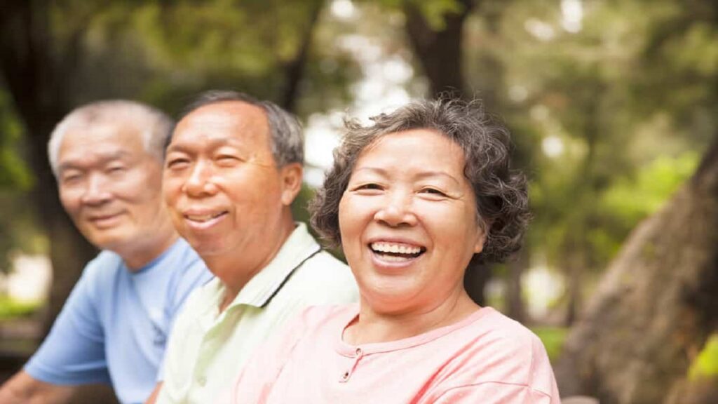 Three smiling seniors sitting together outdoors in a sunny park