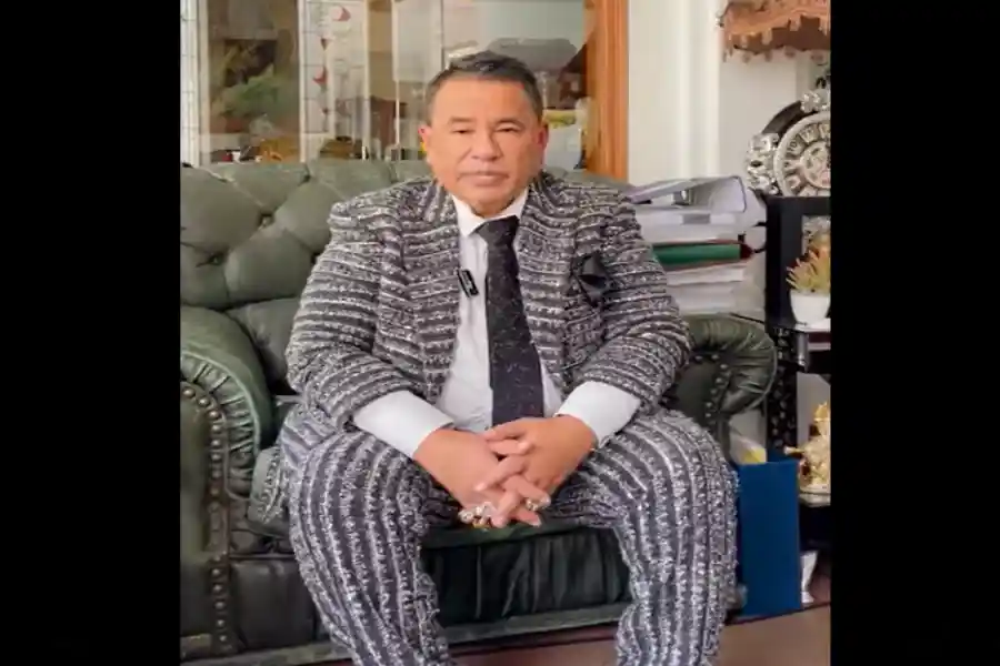 Hotmanparis catrawarta Man in a gray patterned suit sits on a green leather couch hands clasped in his lap in an indoor setting