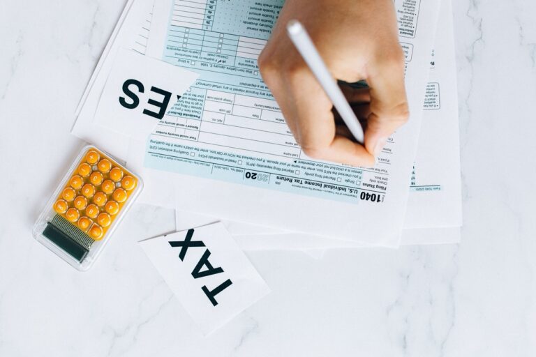 Person writes on tax forms at a marble desk, with a calculator nearby and a 'TAX' card visible.