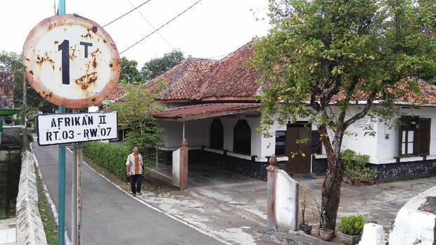 Kampong afrikan catrawarta Rusty road sign with district info near a small building and a tree a person walks along the street in a rural area