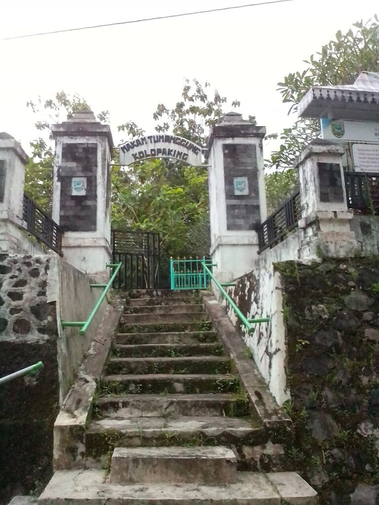 Exifjpeg420 catrawarta Stone mossy staircase with green handrails leading up to a gated archway at a stone entrance surrounded by trees and stone walls sign above the arch is not legible