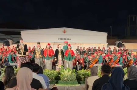Traditional musicians and dancers in colorful outfits perform on an outdoor stage at night with an audience seated in front
