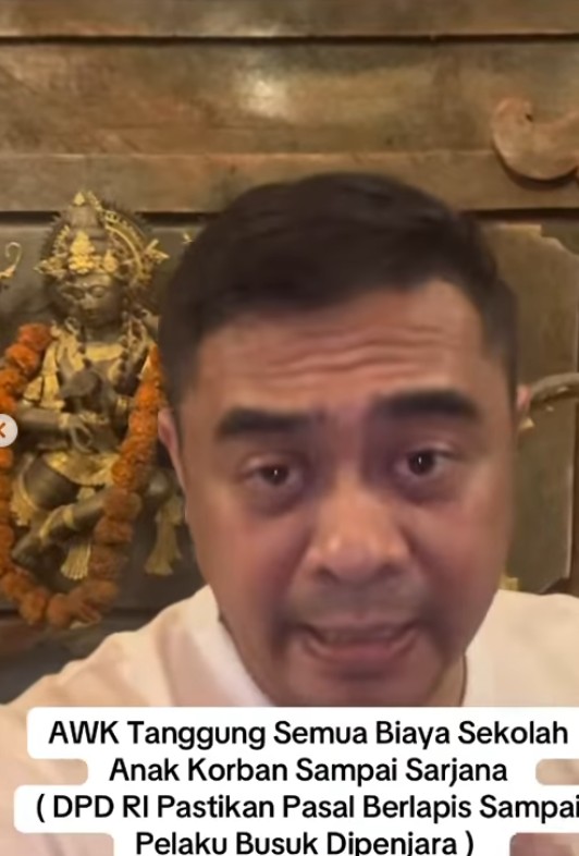 Close up of a man speaking to the camera with a hindu statue in the background and an indonesian caption about covering school expenses