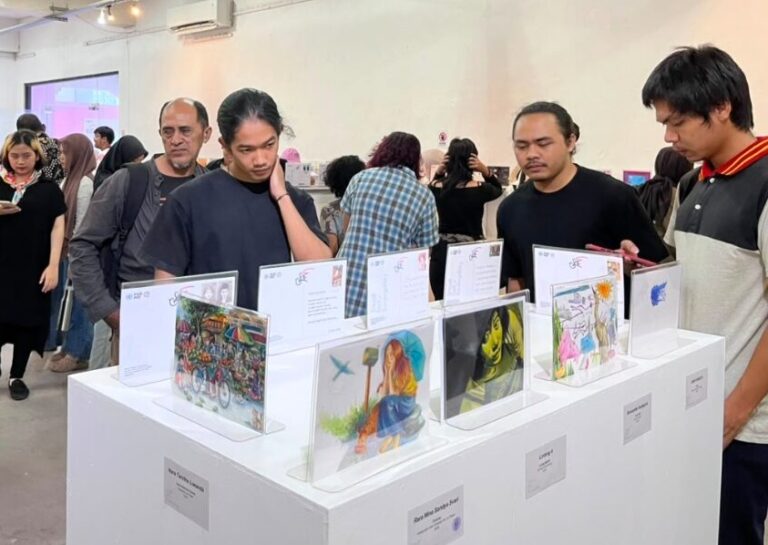 Visitors examine colorful artworks displayed on white pedestals at an art exhibition in a bright gallery setting with a busy crowd
