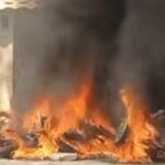 A pile of burning tires and debris in front of a beige building with thick black smoke rising from the flames