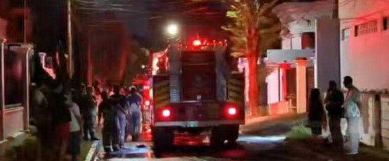 Nighttime street scene with a fire truck and responders, while a crowd watches from the sidewalks.