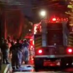 Nighttime street scene with a fire truck and responders while a crowd watches from the sidewalks