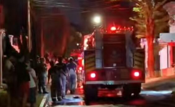 Nighttime street scene with a fire truck and responders while a crowd watches from the sidewalks
