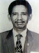 Sutami catrawarta Black and white head and shoulders portrait of a man in a suit and patterned tie facing the camera