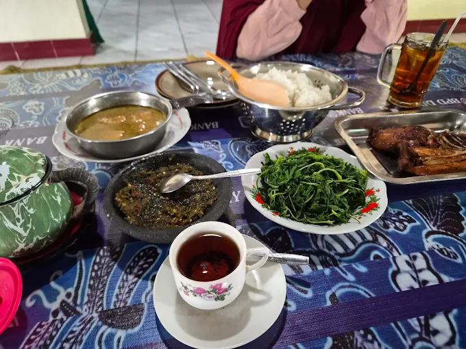 A table spread with rice, greens, curry, and a cup of tea, seen from above as a person sits at the table in the background.
