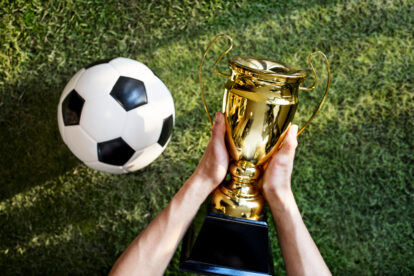 Ilustrasi memegang trofi Piala Dunia 2026 di atas rumput.