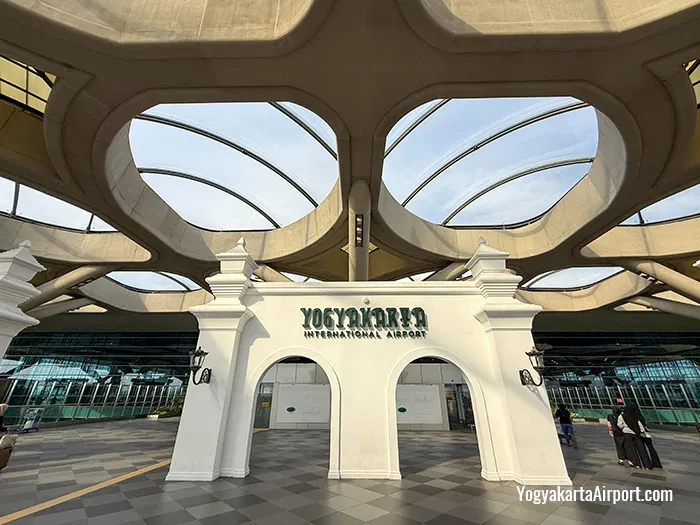 White arched entrance of yogyakarta international airport with bold green signage set under a futuristic curved concrete roof with circular skylight like openings